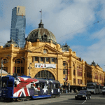 A bustling cityscape with a prominent clock tower, surrounded by a crowd of people. Melbourne cab service in the foreground.